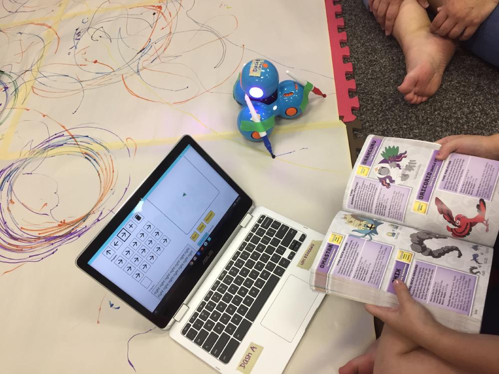 Young learner holding a book and working with a coding environment on their laptop