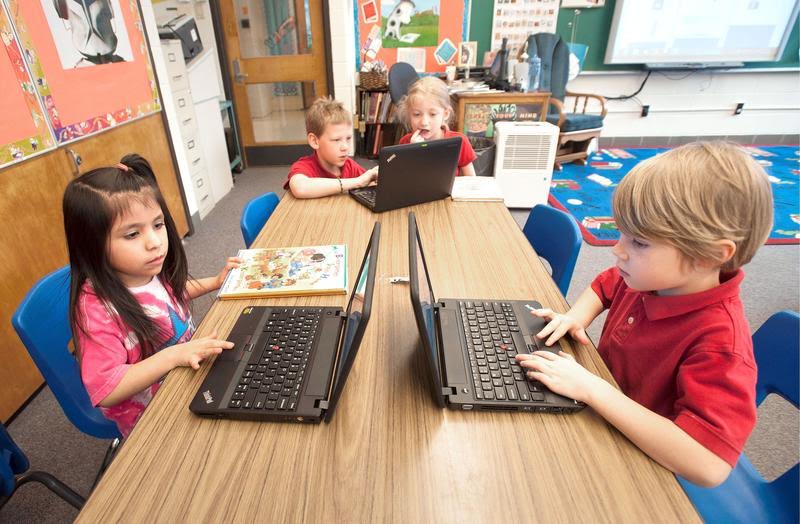 Four young kids sitting around a desk and working with their laptops